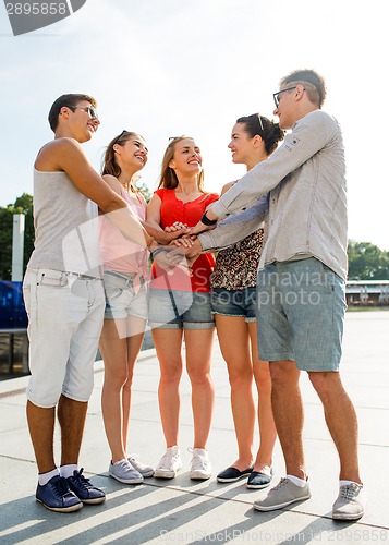 Image of group of smiling friends with hands on top in city