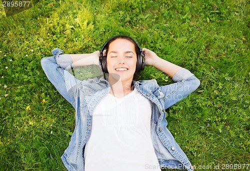 Image of smiling young girl in headphones lying on grass
