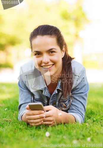 Image of smiling young girl with smartphone lying on grass