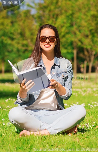 Image of smiling young girl with book sitting in park