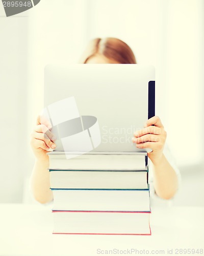 Image of girl hiding behind tablet pc and books at school