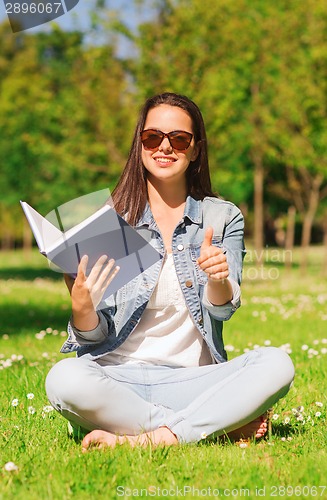 Image of smiling young girl with book sitting on grass