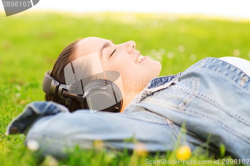 Image of smiling young girl in headphones lying on grass