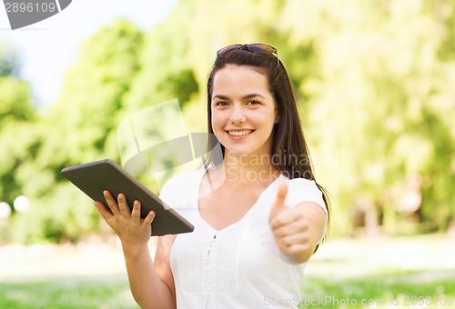 Image of smiling young girl with tablet pc sitting on grass