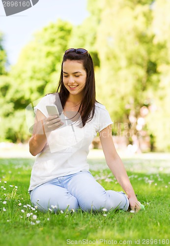 Image of smiling young girl with smartphone sitting in park