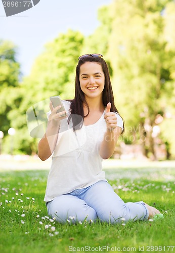 Image of smiling young girl with smartphone sitting in park