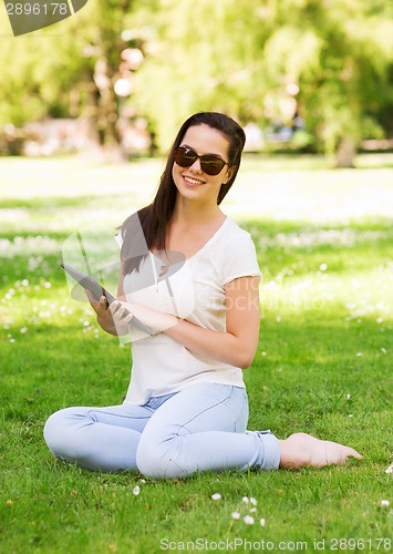 Image of smiling young girl with tablet pc sitting on grass