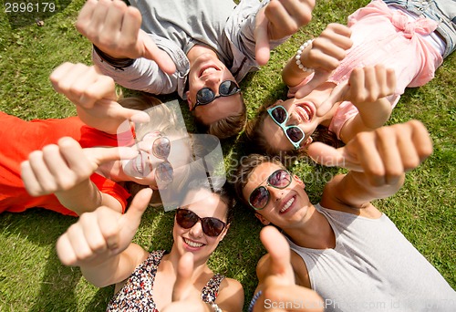 Image of smiling friends showing thumbs up lying on grass