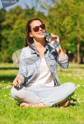Image of smiling young girl with bottle of water in park