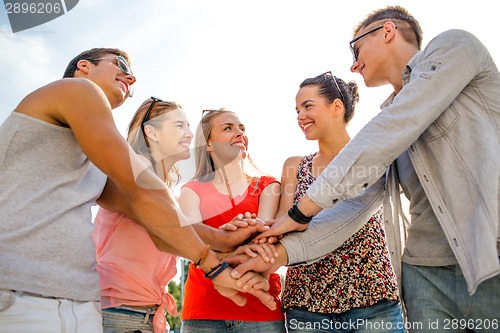 Image of group of smiling friends with hands on top in city