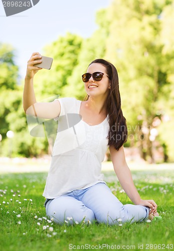 Image of smiling young girl with smartphone sitting in park