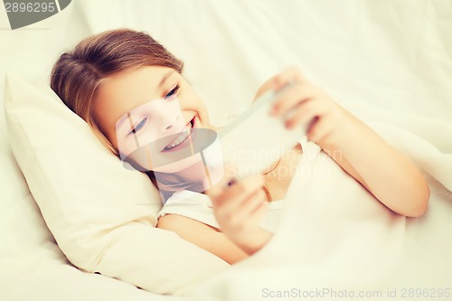 Image of little girl with smartphone playing in bed