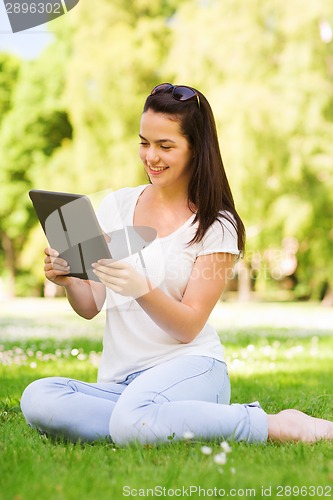 Image of smiling young girl with tablet pc sitting on grass