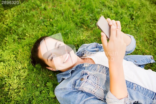 Image of smiling young girl with smartphone lying on grass