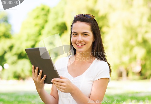 Image of smiling young girl with tablet pc sitting on grass