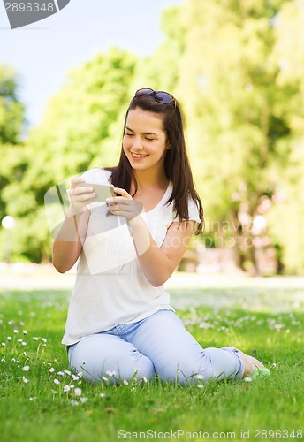 Image of smiling young girl with smartphone sitting in park