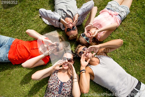 Image of group of smiling friends lying on grass outdoors