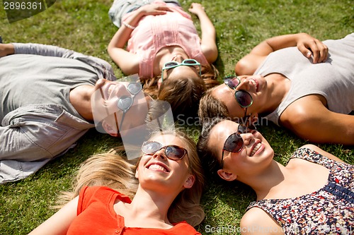 Image of group of smiling friends lying on grass outdoors