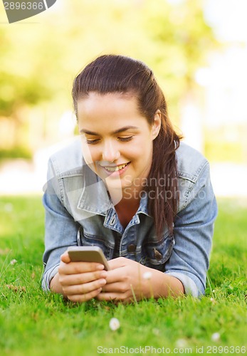 Image of smiling young girl with smartphone lying on grass