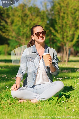 Image of smiling young girl with cup of coffee in park