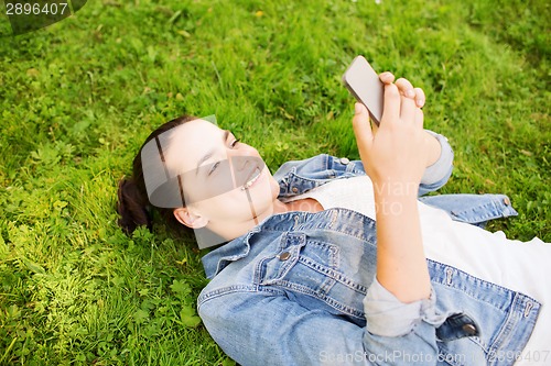 Image of smiling young girl with smartphone lying on grass