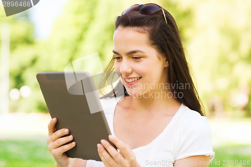 Image of smiling young girl with tablet pc sitting on grass