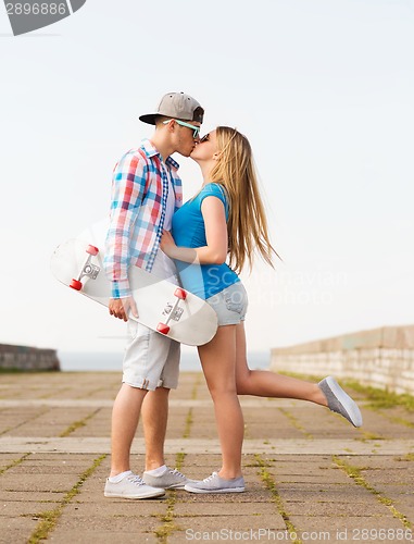 Image of smiling couple with skateboard kissing outdoors