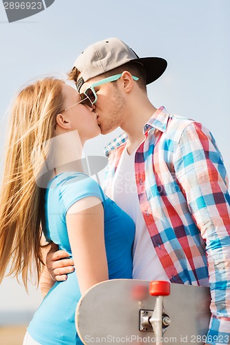 Image of smiling couple with skateboard kissing outdoors