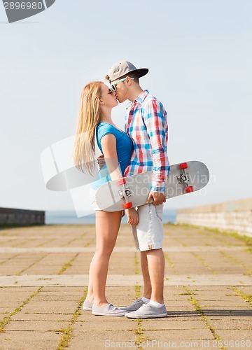 Image of smiling couple with skateboard kissing outdoors