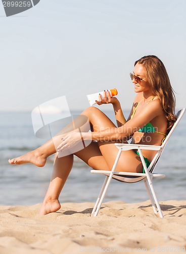 Image of smiling young woman sunbathing in lounge on beach