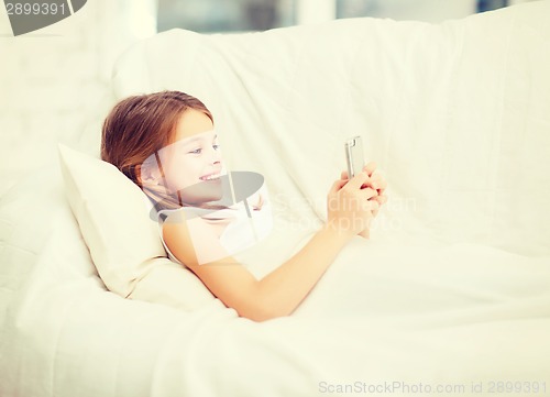 Image of little girl with smartphone playing in bed