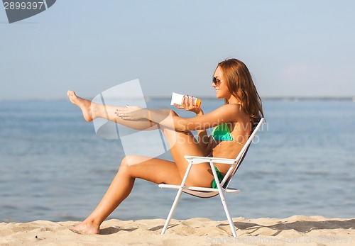 Image of smiling young woman sunbathing in lounge on beach