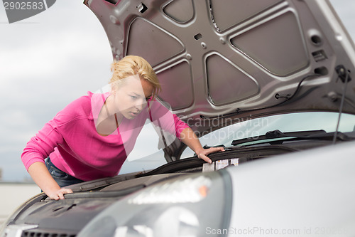 Image of Woman inspecting broken car engine.