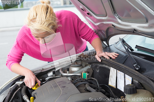 Image of Woman inspecting broken car engine.