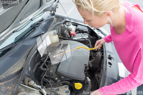 Image of Woman inspecting broken car engine.