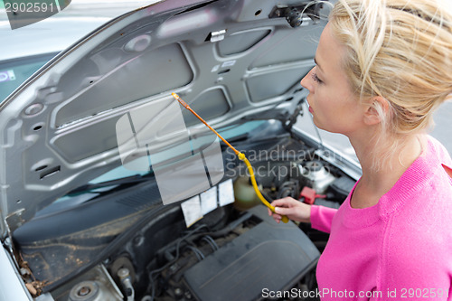 Image of Woman inspecting broken car engine.