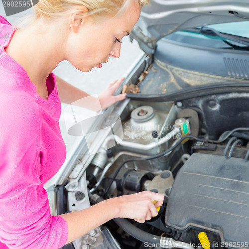 Image of Woman inspecting broken car engine.