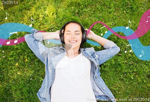 Image of smiling young girl in headphones lying on grass