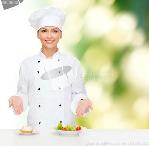 Image of smiling female chef with salad and cake on plates