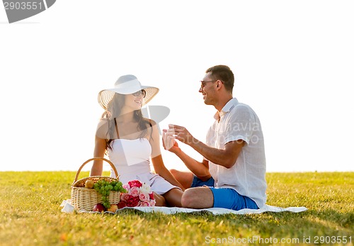 Image of smiling couple with small red gift box on picnic