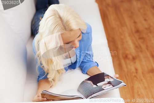 Image of woman lying on couch and reading magazine at home