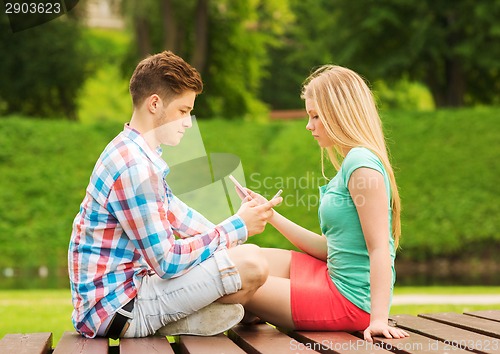 Image of couple with smartphones sitting on bench in park