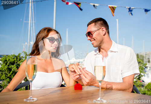 Image of smiling couple with champagne and gift at cafe