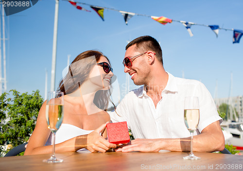 Image of smiling couple with champagne and gift at cafe