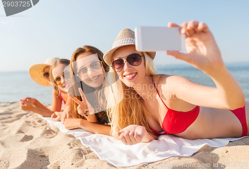 Image of group of smiling women with smartphone on beach