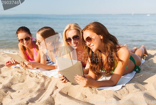 Image of group of smiling young women with tablets on beach