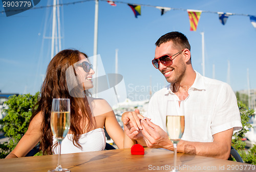 Image of smiling couple with champagne and gift at cafe