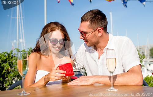 Image of smiling couple with champagne and gift at cafe
