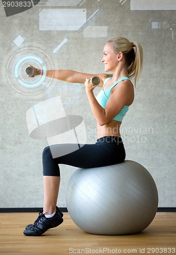 Image of smiling woman with dumbbells and exercise ball