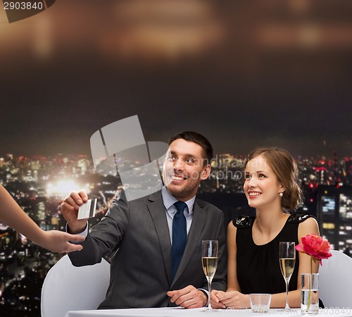 Image of smiling couple paying for dinner with credit card